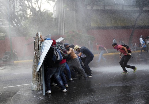 Anti government demonstrators take cover from a police water cannon in Caracas, Venezuela, / AP