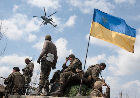 A military Ukrainian Army helicopter flies over a column of Ukrainian Army combat vehicles