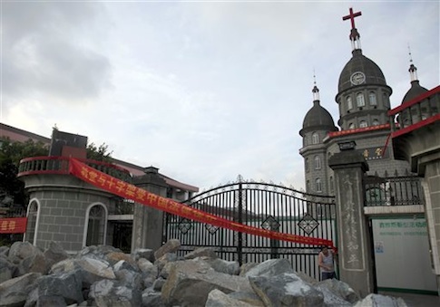 In this photo taken July 16, 2014, a church member of Zengshan Village Christian Church stands near rocks piled up in front of the gate to prevent government workers from moving in equipment to demolish the cross
