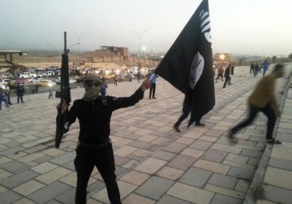 A fighter of the Islamic State of Iraq and the Levant (ISIL) holds an ISIL flag and a weapon on a street in the city of Mosul