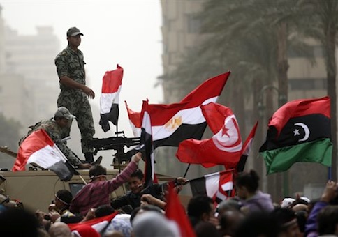 Egyptian army officers guard on top of an armored vehicle as demonstrators wave the Egyptian, Tunisian and Libya's old national flags