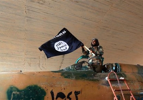 This undated image posted on Aug. 27, 2014 by the Raqqa Media Center of the Islamic State group, a Syrian opposition group, which has been verified and is consistent with other AP reporting, shows a fighter of the Islamic State group waving their flag from inside a captured government fighter jet
