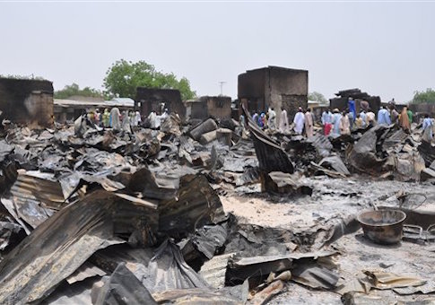 In this Sunday, May 11, 2014 file photo, people stand outside burnt houses following an attack by Islamic militants in Gambaru, Nigeria. Thousands of members of Nigeriaís home-grown Islamic extremist Boko Haram group strike across the border in Cameroon, with coordinated attacks on border towns, a troop convoy and a major barracks.