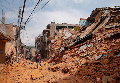 A youth carries his belongings on his back as he walks through destroyed houses in Sindhupalchowk district