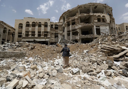 Houthi militant walks in front of a government compound, destroyed by recent Saudi-led air strikes, in Yemen's northwestern city of Amran