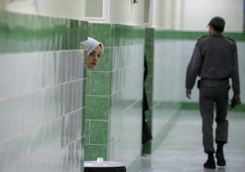 An Iranian inmate peers from behind a wall as a guard walks by at the female section of the infamous Evin jail