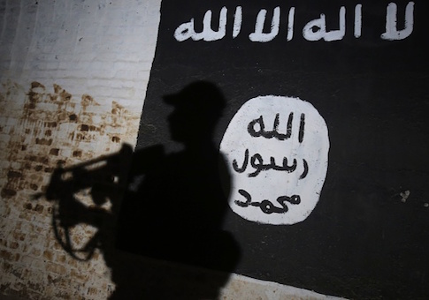 A member of the Iraqi forces walks past a mural bearing the logo of the Islamic State