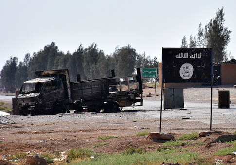 A general view shows a burnt out vehicle next to a banner bearing the Islamic State group's flag
