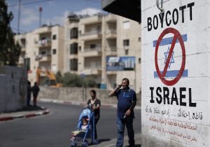 Palestinians walk past a sign painted on a wall calling to boycott Israeli products coming from Jewish settlements