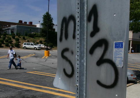 An unidentified man walks with a young boy thru a grocery store parking lot near a traffic sign with the back of it spray painted indicating it as territory for the El Salvaldorian gang MS13 in the Washington, DC, suburb of Silver Spring, Maryland