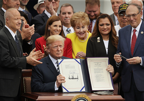Donald Trump holds up the Veterans Affairs Mission Act he signed