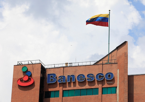 A Venezuelan flag waves above the corporate logo of Banesco bank at one of their office complexes in Caracas