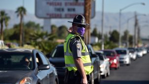 A Nevada Highway Patrol officer directs vehicles as they wait to get into a drive-thru food distributing site