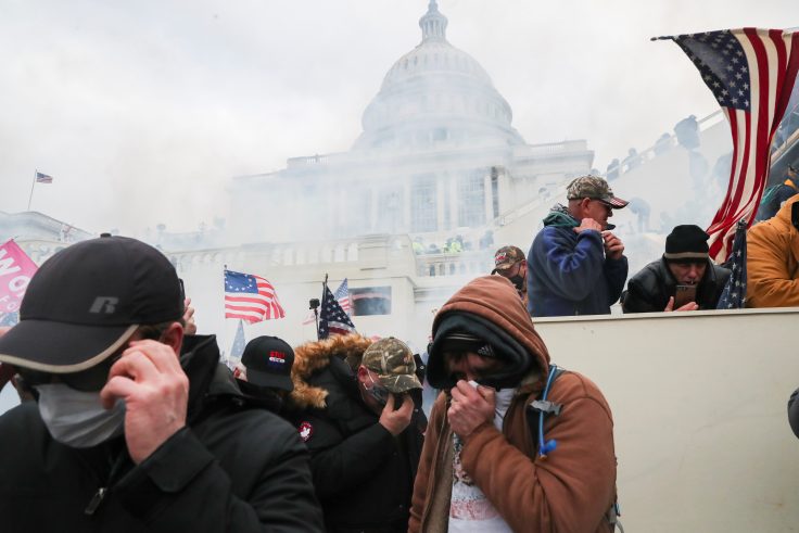 Supporters of U.S. President Donald Trump cover their faces to protect from tear gas during a clash with police officers in front of the U.S. Capitol Building