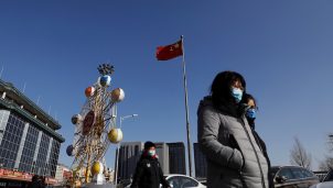 People wearing face masks walk past a Chinese flag, following new cases of the coronavirus disease (COVID-19) in the country, in Beijing